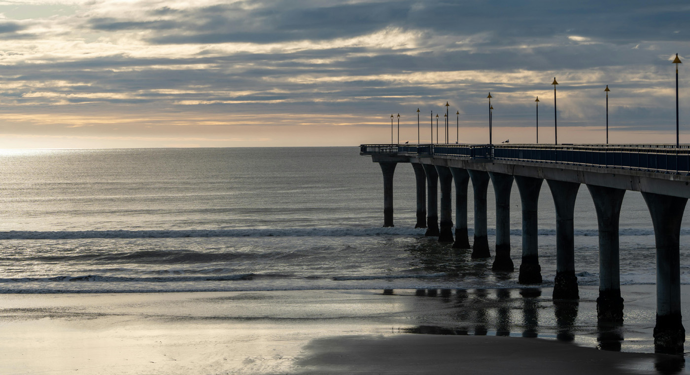 Wide shot of a beach and the ocean with a wharf off to the right side