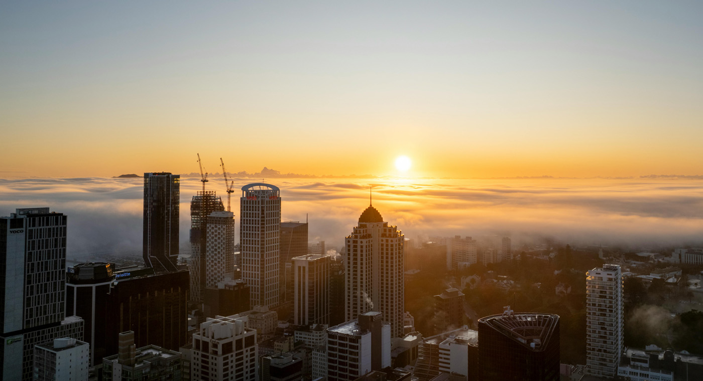 Wide shot of city skyline, with a sun setting in the background