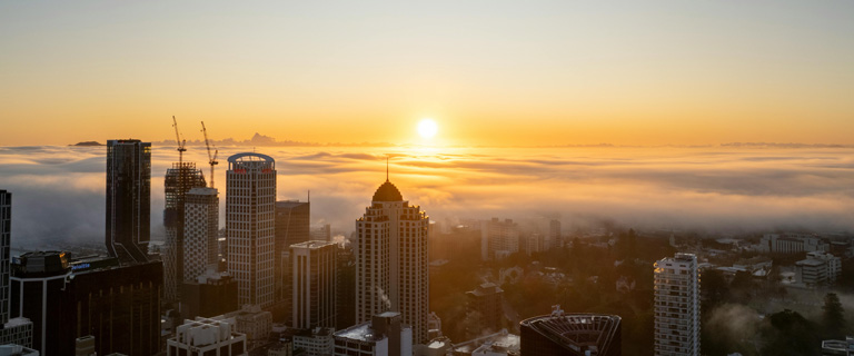 Wide shot of city skyline, with a sun setting in the background